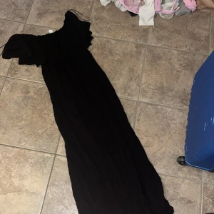 Svart långklänning från Divided - Supersnygg svart långklänning från Divided med offshoulder och volang upptill. Klänningen är luftig och har en flowy passform, perfekt för sommarkvällar. Materialet känns lätt och bekvämt mot huden.