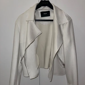 Vit jacka från Bik Bok - Snygg vit jacka från Bik Bok i storlek S. Jackan har klassisk krage, sned dragkedja och silvriga detaljer vid axlar. Materialet är slätt och ger en clean look. Perfekt för dig som vill ha en stilren och trendig jacka till din outfit.