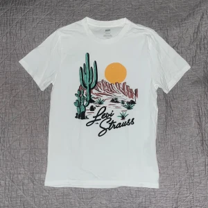 Vit Levi's t-shirt med tryck - Vit t-shirt från Levi's med coolt tryck av kaktusar, berg och sol i färg på framsidan. Klassisk passform och rund hals. Perfekt för dig som gillar streetstyle och grafiska prints.