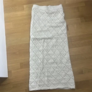 Vit långkjol virkad - Superfin vit långkjol med virkat mönster i bomull. Kjolen har ett diskret hålmönster i rutigt och är perfekt för varma dagar. Den har en rak passform och bred midjeresår för extra komfort. Enkel att styla med både toppar och sneakers.
