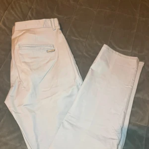 Ljusgrå kostymbyxor Calvin Klein - Snygga ljusgrå kostymbyxor från Calvin Klein med klassisk passform. Byxorna har raka ben, diskreta fickor och en stilren metallogo bak. Perfekta för dig som gillar en clean och modern look.