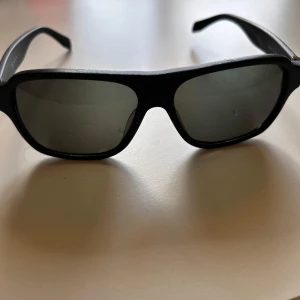 Svarta solglasögon från Alexander McQueen - Stilrena svarta solglasögon från Alexander McQueen med klassisk bågform och mörka glas. Snygg logotyp på skalmen och robust plastmaterial. Perfekta för att ge en cool touch till din look. Nypris 2000kr. Priset är runt 200 pga finns ingen box eller kvitto