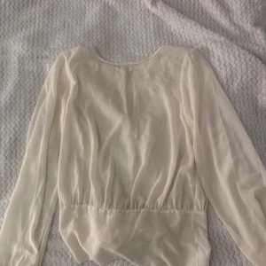 Vit blus med knyt från Vila - Supersöt vit blus från Vila i luftig och lätt polyester. Blusen har långa ärmar, rund halsringning och en snygg knytning framtill i midjan. Perfekt för dig som gillar en feminin och stilren look. Stängs med knapp i nacken.