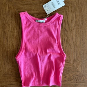 Rosa ribbad linnetopp från Zara - Säljer en snygg rosa ribbad linnetopp från Zara. Toppen är croppad och har breda axelband och rund halsringning. Perfekt för sommaren och enkel att matcha med jeans eller kjol. Aldrig använd 