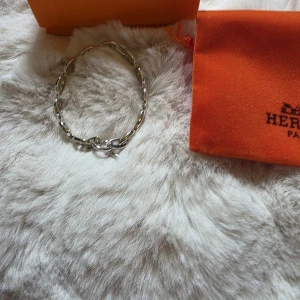 Silverarmband  - Säljer ett exklusivt armband från i silver. Armbandet har klassiska kedjelänkar med med signaturdesign och T-lås. Perfekt accessoar för att lyfta din stil med en lyxig touch. Kan inte nämna märket då Plick tar bort annonsen, trots stämpel och serienummer. Se bilder.