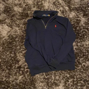 Mörkblå tröja från Ralph Lauren - Säljer en stilren mörkblå tröja från Ralph Lauren med dragkedja och röd broderad logga på bröstet. Tröjan har långa ärmar och en hög krage, perfekt för kyligare dagar. Skick 8/10 inga hål använd några gånger. Pris 650 kan diskuteras vid snabb affär storlek S hör av vid minsta fråga eller pris !