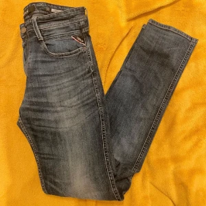Replay Anbass jeans, blå, W32 L34 - Säljer ett par Replay Anbass jeans i klassisk blå tvätt med snygga slitningar. Modellen har fem fickor, raka ben och normal passform. Jeansen är tillverkade i bomull och har Replay-logga på fickan och bak på linningen. Den har ett litet hål vid gylfen men man ser inte de och de går att fixa