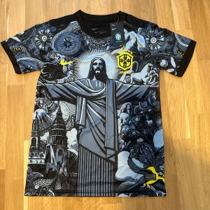 Nike Brasil Dri-Fit t-shirt med tryck - Snygg svart och grå Nike Dri-Fit t-shirt med Brasil-logga och stort grafiskt tryck av Kristusstatyn och Rio-motiv. Unik design med detaljer i gult och blått, korta ärmar och sportig känsla. Perfekt för dig som vill sticka ut med streetstyle och fotbollsvibe.