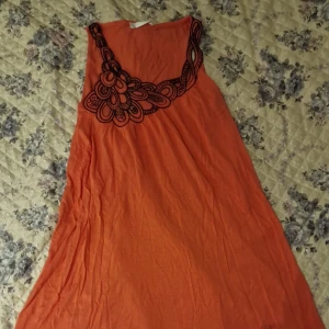 Orange ärmlös klänning från Promod - Säljer en orange ärmlös kort klänning från Promod med svart broderad detalj längs ena axeln och halsringningen. Klänningen har en lös passform och är perfekt för varma dagar.