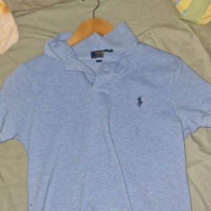 Ljusblå pikétröja från Polo Ralph Lauren - Säljer en klassisk ljusblå pikétröja från Polo Ralph Lauren med broderad logga på bröstet. Tröjan har korta ärmar och krage med knappar. Perfekt för en avslappnad och stilren look.