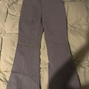 Grå kostymbyxor från Gina Tricot - Snygga grå kostymbyxor från Gina Tricot med klassisk passform och vida ben. Byxorna har hällor för bälte och är tillverkade i ett mjukt material som känns bekvämt hela dagen. Perfekta för en stilren look. Använda en gång