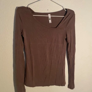 Brun långärmad tröja med asymmetrisk halsringning - Säljer en brun långärmad topp med en snygg asymmetrisk halsringning. Tunn och stretchig modell som sitter tight och passar perfekt till jeans eller kjol. Enkel och stilren design utan mönster eller detaljer.💞
