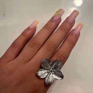 Stor silverfärgad blomring - Säljer en statementring i silverfärg med en stor, detaljerad blomma som motiv. Ringen har justerbar storlek och blommans blad har fina räfflade detaljer som ger en cool 3D-effekt. Perfekt accessoar för dig som vill sticka ut med din stil.