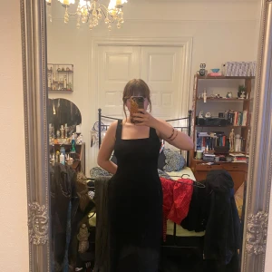 Svart långklänning med broderi - Säljer en svart långklänning med breda axelband och fyrkantig urringning. Klänningen har vackra svarta broderade blommor framtill och en diskret slits bak. Perfekt för dig som gillar stilrena och unika detaljer.