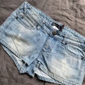 Ljusblå lowwaist jeansshorts från ONLY - Säljer dessa populära snygga lowwaist jeansshorts från ONLY med klassisk femficksdesign och knappgylf. De är i storlek W28 och har jättesnygga slitningar på framsidan och unika korsade bälteshylsor! 