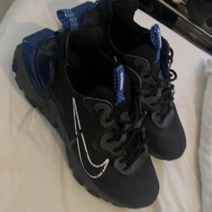 Nike Air Max sneakers svart/blå - Säljer ett par svarta Nike Air Max sneakers med blå detaljer och vit swoosh på sidan. Skorna har en robust sula och snörning framtill. Perfekta för dig som gillar sportig stil och vill ha något bekvämt till vardags. Har boxen till skorna 