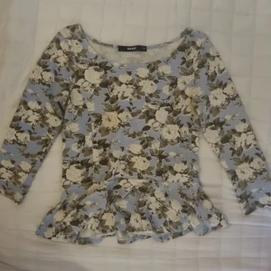 Super gullig och fin sommartopg topp med volang från Bik Bok. - Supersöt topp från Bik Bok i ljusblått med blommigt mönster i vitt och beige. Modellen har korta  ärmar och en volang nertill som ger en extra feminin touch. Perfekt för dig som gillar iconic stil l och vill sticka ut lite extra. Köpt begagnat men jag själv har använt den typ 2 gånger.