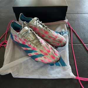 Adidas fotbollsskor med blå och rosa detaljer - Säljer ett par Adidas fotbollsskor i vitt med blå undersula skorna är lite söndriga vid tårna på båda skorna men perfekt om du är en mittback/målvakt Skriv i till mig för fler bilder. Skorna är i storlek 47. Pris går och diskutera.😀