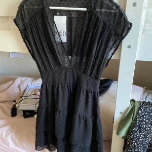 kortklänning med v-ringning från Zara - Supersnygg svart kortklänning från Zara med djup v-ringning och transparenta detaljer. Klänningen har korta ärmar, volanger och ett diskret prickigt mönster i tyget. Perfekt för dig som vill ha en trendig och luftig look. 