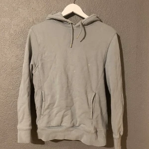 Grå hoodie från H&M - Säljer en stilren grå hoodie från H&M. Den har en klassisk design med dragsko i huvan och fickor framtill. Perfekt för en avslappnad look. Passar bra till både jeans och joggers.