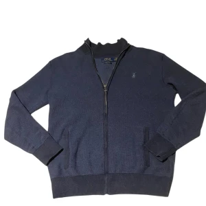 Mörkblå tröja med dragkedja från Ralph Lauren - Säljer en stilren mörkblå tröja från Ralph Lauren i bomull. Tröjan har en dragkedja framtill och långa ärmar. Perfekt för en avslappnad och snygg look. Passar bra till både jeans och chinos.