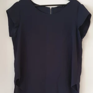 Mörkblå blus med dragkedja - Snygg mörkblå blus med korta ärmar och rund halsringning. Blusen har en dragkedja i ryggen. 