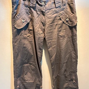 Beige cargopants med fickor - Snygga beige cargopants med flera praktiska fickor och knappdetaljer. Byxorna har en loose passform och är perfekta för en avslappnad stil. Tillverkade i ett slitstarkt material som passar bra för vardagsbruk.