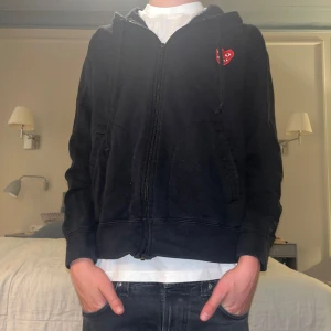 Svart hoodie från Comme des Garçons Play - Säljer en sjukt snygg svart hoodie från Comme des Garçons Play med dragkedja och det ikoniska röda hjärtemärket. Modellen i bilden är 178, så passformen är mer mot S sidan. Original pris är 2500 kr men säljs endas för 799 kr! Skick är 8/10, och pris kan diskuteras.🔥🔥