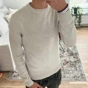 Vit stickad tröja från Dobber - Säljer en stilren vit stickad tröja från Dobber. Tröjan har en klassisk rund hals och långa ärmar med ribbade muddar. Perfekt nu inför våren. Den har inga som helst defekter. Jag är 180 lång 