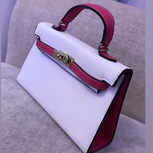 Vit och rosa handväska - Snygg handväska i vitt och rosa med ett elegant handtag och guldfärgad låsdetalj. 