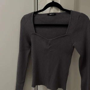 RIBBAD TOPP - GinaTricot - Snygg grå ribbad tröja från Gina Tricot med långärmad design. Perfekt för en stilren look med en v-ringad halslinje som ger en modern touch. Tröjan har användts 2 gånger och den är väldigt bekväm och mysig. Jag säljer den eftersom jag inte användt den och tycker ej den passar tillsammans med min klädstil 🩶