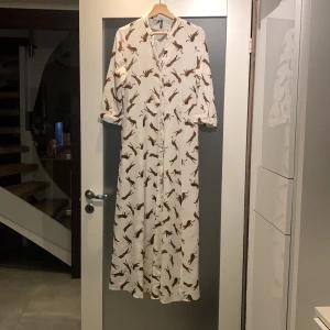 Vit långklänning med leopardmönster från Vero Moda - Säljer en vit långklänning från Vero Moda med coolt leopardmönster. Klänningen har trekvartsärmar och en avslappnad passform. Perfekt för dig som vill sticka ut med stil! 🐆