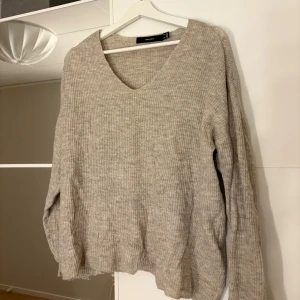 Beige stickad tröja från Vero Moda - Mysig beige stickad tröja från Vero Moda med v-ringning. Hör av er vid funderingar eller om ni vill ha bilder med hur plagget sitter på mig. Titta gärna in mina andra plagg!. Tröjan har långa ärmar och en neutral färg som passar till det mesta.