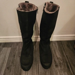 Svarta vinterstövlar från Canada Snow - Snygga svarta stövlar från Canada Snow med dragkedja och mjukt foder av lammull. Perfekta för kalla vinterdagar. Tillverkade i Portugal med hög kvalitet och komfort i åtanke.