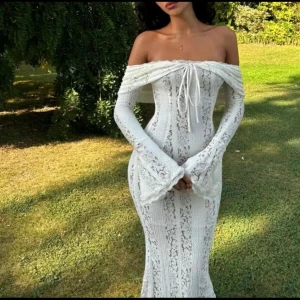 Vit spetsklänning - Elegant vit långklänning i spets med offshoulder-design och långa ärmar. Klänningen har en åtsittande passform och vackra detaljer som knytning framtill. Perfekt för speciella tillfällen.nypris 3300. Använd en gång