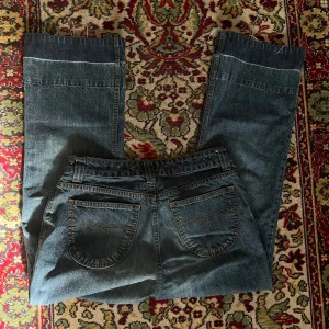 Blå jeansbyxor - midwaist bootcut jeans med cool broderi på fickorna och design ner till benen från gamla lindex    midjemått rakt av: 38cm. innerbenslängd: 70cm