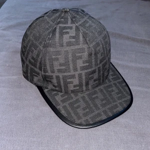 Grå keps från Fendi - Snygg grå keps från Fendi med ett stilrent mönster. Kepsen har en  justerbar rem baktill för perfekt passform. Perfekt för att ge din outfit en lyxig touch. top kvalite, skick 10/10