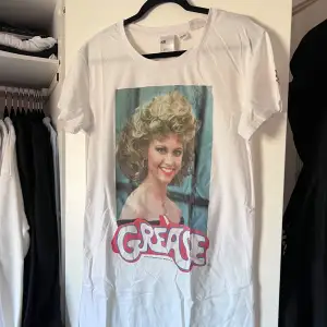 Säljer ett vitt nattlinne från H&M med ett stort tryck av karaktären Sandy från filmen Grease på framsidan. Nattlinnet har korta ärmar och en rund halsringning. Perfekt för filmälskare och retrostil! 🎬 Önskar du veta exakta mått? Tveka inte att höra av dig!