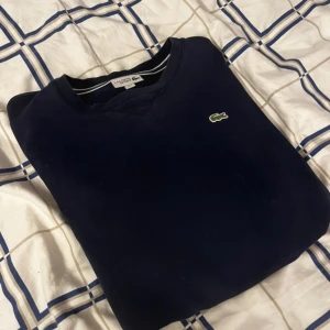 Mörkblå tröja från Lacoste Sport - Säljer en stilren mörkblå tröja från Lacoste Sport med det klassiska krokodilemblem på bröstet. Tröjan har en rund halsringning och är perfekt för en avslappnad look.