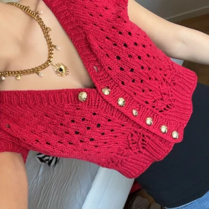 Röd stickad bolero med gulddetaljer - Säljer en snygg röd stickad bolero med korta ärmar och dekorativa guldknappar. Koftan har ett hålmönster och ribbade kanter som ger en trendig look. Perfekt för att lägga till en färgklick i din garderob!Intressekoll därför går det inte att köpa direkt, om många är intresserade kommer jag lägga ut en ny annons där det går att köpa direkt😊