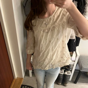 Beige blus från Noa Noa - Charmig beige blus från Noa Noa med vackra broderade detaljer och trekvartsärmar. Blusen har en rund halsringning och knappar i ryggen. Perfekt för en elegant och avslappnad stil.