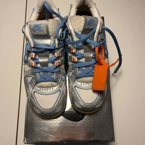 Nike Air Rubber Dunk - Snygga Nike Air Rubber Dunk med en unik design i vitt och blått. Skorna har blå snörning och en orange tagg som ger en cool kontrast. Perfekta för dig som vill ha något annorlunda i skogarderoben. Säljer dessa då dom blivit för små för mig. Köpt för 6000 säljer för 3000