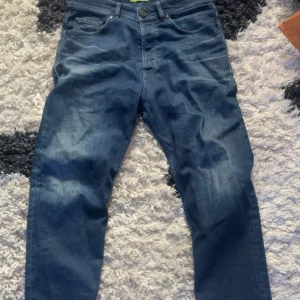 Blå jeans från Versace Jeans - Snygga blå jeans från Versace Jeans med en broderad logga på bakfickan. Klassisk femficksdesign med knapp och dragkedja framtill. Perfekta för en stilren look.