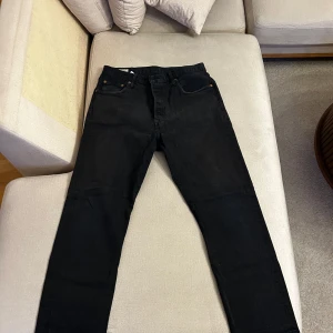 Svarta jeansbyxor från Levi's - Snygga svarta jeansbyxor från Levi's med klassisk femficksdesign och knappgylf. Perfekta för en stilren look. Levi's logotyp syns på bakfickan.