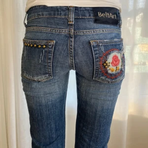 Unika lågmidjade jeans - Unika lågmidjade jeans från BeltArt med broderad rosdetalj på bakfickan och nitar. Midjemått- 40cm Innerbenslängd- 90cm