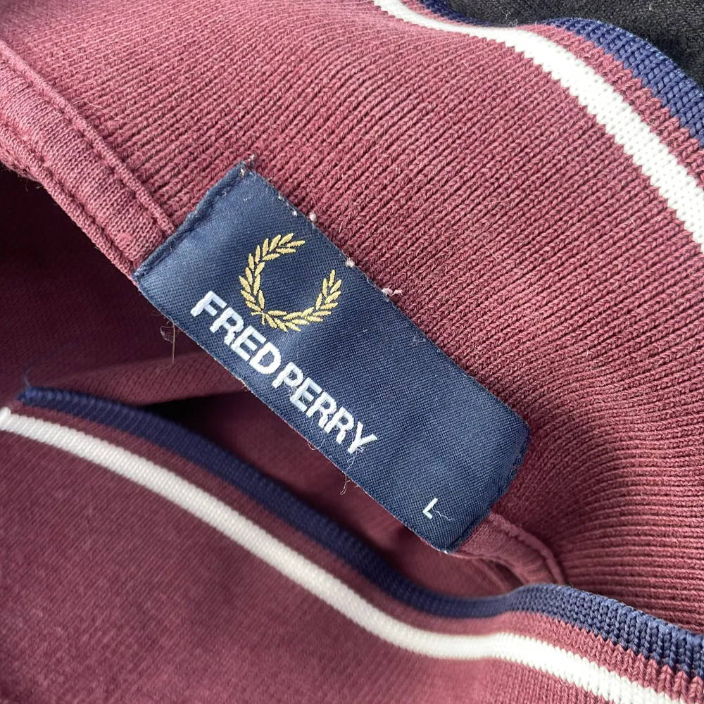 Säljer en snygg vinröd pikétröja från Fred Perry med klassisk krage och knappar. Tröjan har vita och blå ränder på krage och ärmslut, vilket ger en stilren look. Perfekt för en avslappnad stil.. T-paidat.
