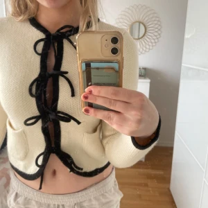Beige stickad kofta från Zara - Säljer en beige stickad kofta från Zara med svarta detaljer och knytband framtill. Koftan är croppad och har långa ärmar samt två små fickor. Perfekt för en trendig look! Är super söt men säljer pga det nt är min smak längre💞helt ny har använts en gång 💞