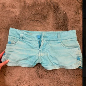 Lågmidjade vintage shorts - Snygga ljusblå vintage shorts med knappar framtill och på sidorna. De har blommor mönster på insidan. Midjemåttet är 39 cm och längden på shortsen är ca 20cm fram. Hör av er vid funderingar och titta gärna in mina andra plagg!
