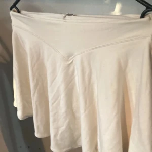 Vit kortkjol från Oh Polly - Supersöt vit kortkjol från Oh Polly med v-format midjeband. Kjolen är lätt utsvängd och har en enkel, clean look som passar perfekt till sneakers eller boots. Mjuk och skön i bomullsmaterial, perfekt för varmare dagar.