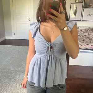 Ljusblå blus med volang🩵 - Supersöt ljusblå blus från Lager 157 med volangärmar och knytning framtill. Toppen har v-ringning, smockat tyg och en flowy, luftig passform. Funkar både till vardags men också om du ska klä upp dig💞 Knappt använd